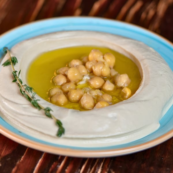Creamy hummus with a pool of olive oil, chickpeas, and a sprig of thyme in a blue-rimmed bowl.