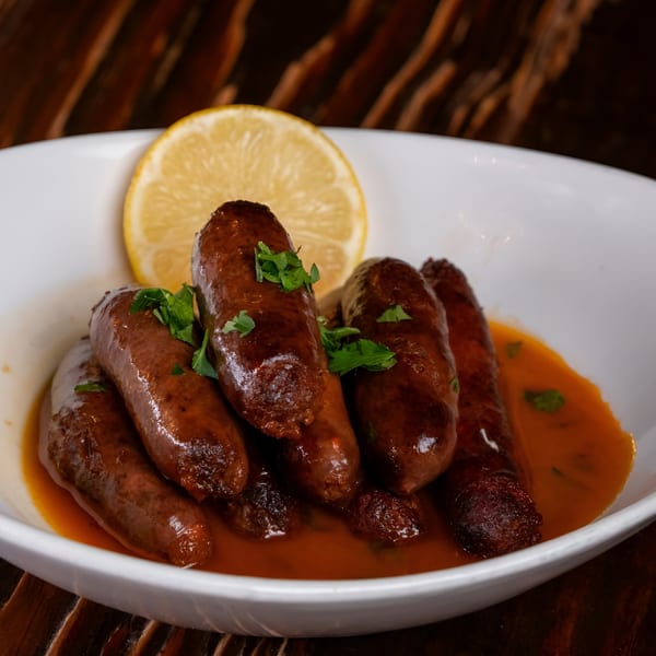 Sirocco's Mediterranean sausages in a rich sauce, garnished with parsley and a lemon slice.