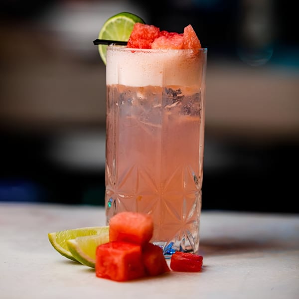 A refreshing watermelon cocktail with lime and watermelon cubes on a white surface.