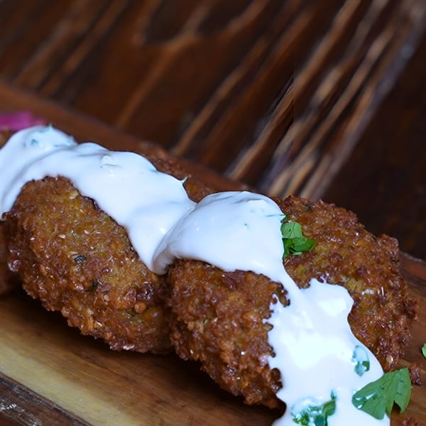 Crispy falafel patties drizzled with creamy white sauce and garnished with fresh herbs on a wooden board.