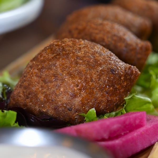 Close-up of golden-brown kibbeh on a bed of lettuce with pink pickled vegetables.