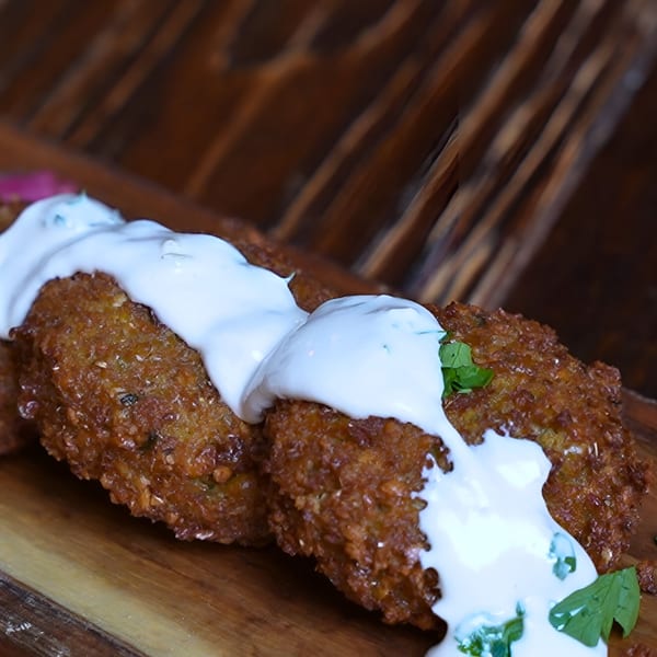 Crispy golden-brown falafel patties topped with a creamy white sauce and fresh green herbs on a wooden board.