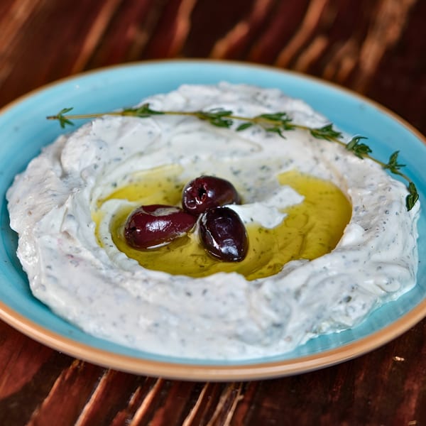 Creamy Mediterranean dip with a pool of olive oil, three dark olives, and a sprig of thyme.