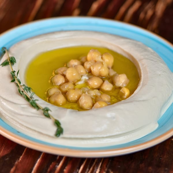 Creamy hummus topped with chickpeas, olive oil, and a sprig of thyme in a blue-rimmed bowl.