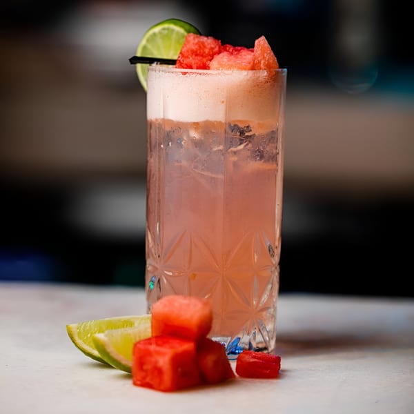 A refreshing watermelon cocktail, garnished with fresh lime and watermelon cubes, on a light surface.
