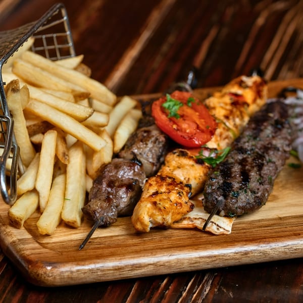 Sirocco's Mediterranean mixed grill with beef, chicken, and kofta kebabs, fries, and tomato on a wooden board.