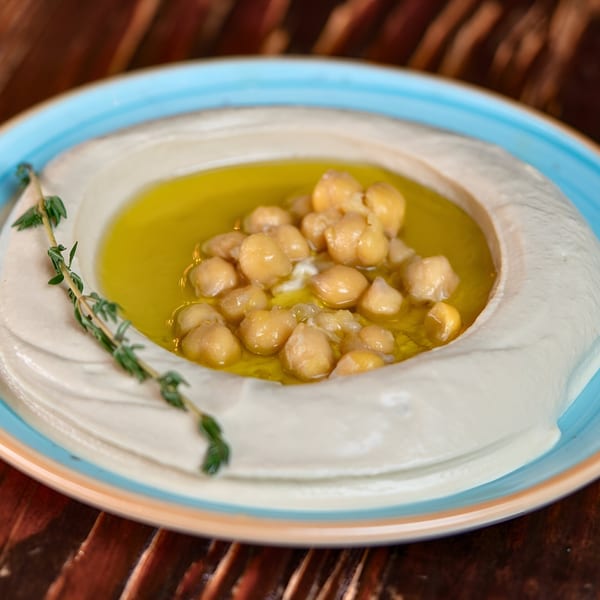 Creamy hummus topped with chickpeas, olive oil, and a sprig of thyme in a blue-rimmed bowl.