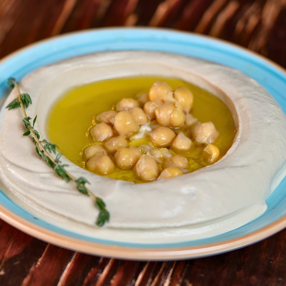 Creamy hummus topped with chickpeas, olive oil, and a sprig of thyme in a blue-rimmed bowl.