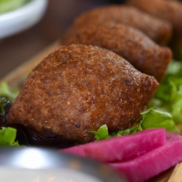 Close-up of golden-brown kibbeh on a bed of lettuce with bright pink pickled turnips.