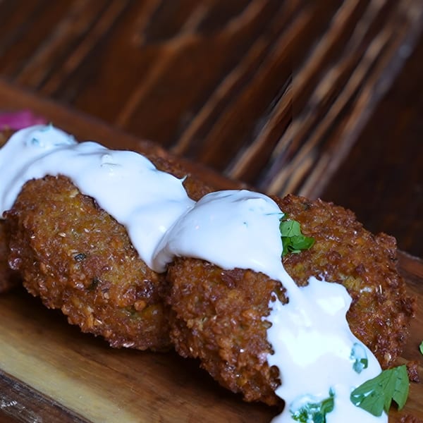 Crispy falafel patties drizzled with white sauce and garnished with fresh herbs on a wooden board.